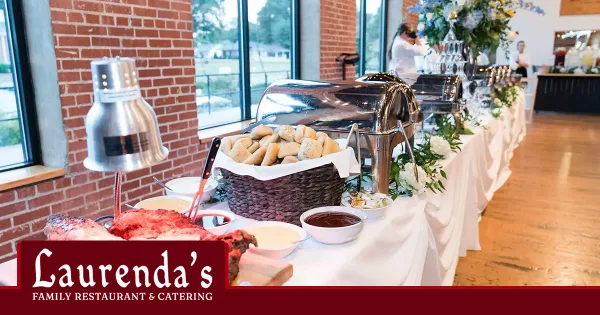 A catering buffet table featuring chafing dishes, a basket of rolls, and a brick wall background, with the Laurenda's Family Restaurant & Catering logo in the corner.