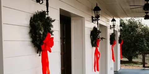 White venue porch with black lanterns, holiday wreaths with red ribbons, and outdoor greenery visible in the background.