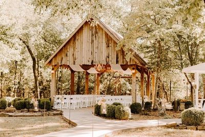 Outdoor wooden chapel structure with white chairs and a floral arch set among trees