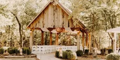 Outdoor wooden chapel structure with white chairs and a floral arch set among trees