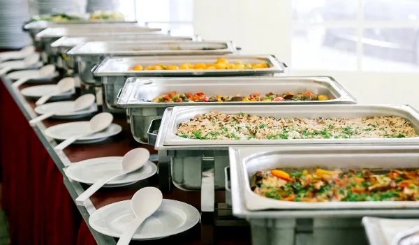 A catering buffet line featuring several stainless steel chafing dishes filled with various prepared meals and side dishes.