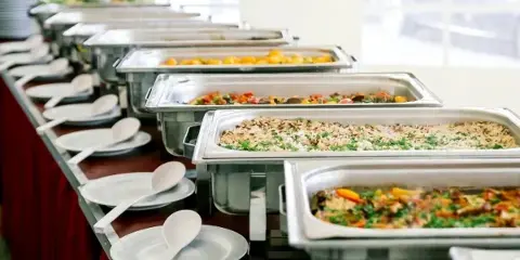 A catering buffet line featuring several stainless steel chafing dishes filled with various prepared meals and side dishes.