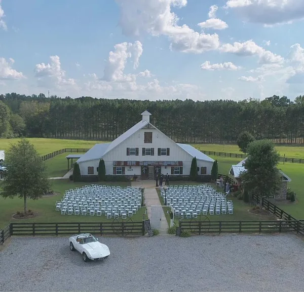 Aerial view of a white barn wedding venue with rows of white chairs set up for a ceremony on the lawn.