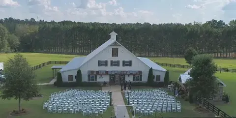 Aerial view of a white barn wedding venue with rows of white chairs set up for a ceremony on the lawn.