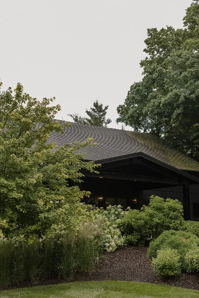 Exterior view of a dark-roofed barn structure surrounded by lush greenery and manicured landscaping.