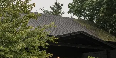 Exterior view of a dark-roofed barn structure surrounded by lush greenery and manicured landscaping.