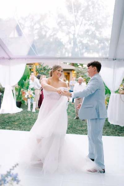 A bride and groom dancing under a semi-clear top tent at an outdoor wedding venue.