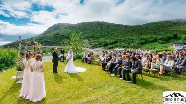 Outdoor wedding ceremony on a grassy lawn with a mountain backdrop and seated guests.