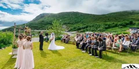 Outdoor wedding ceremony on a grassy lawn with a mountain backdrop and seated guests.