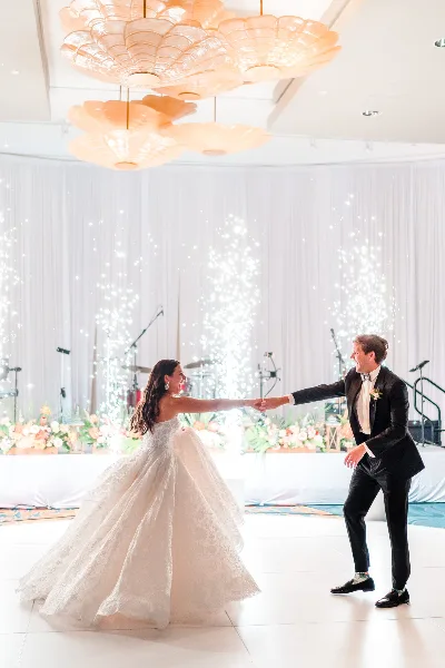 A bride and groom dancing at a wedding reception under large decorative chandeliers.