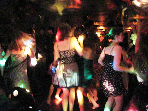 A crowded dance floor with people dancing under colorful lights.