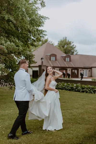 A bride and groom laughing on the lawn in front of a large French provincial style mansion.