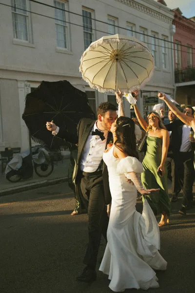 A bride and groom dancing in a street with guests holding parasols.