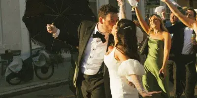 A bride and groom dancing in a street with guests holding parasols.