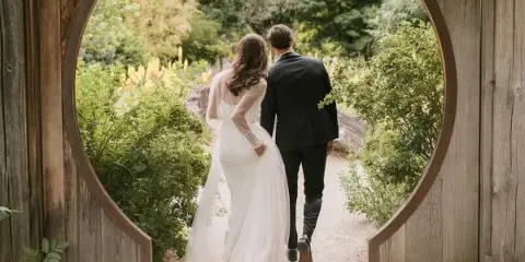 A bride and groom walking away from the camera through a circular wooden garden archway.