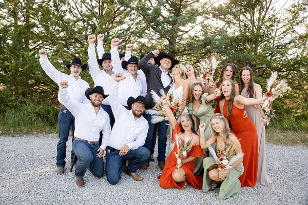 A wedding party consisting of a bride, groom, and attendants posing together outdoors on a gravel path.
