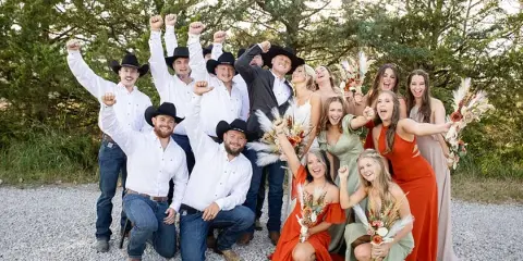 A wedding party consisting of a bride, groom, and attendants posing together outdoors on a gravel path.