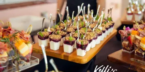 A catering table featuring rows of individual dessert cups and appetizers with a staff member in the background.