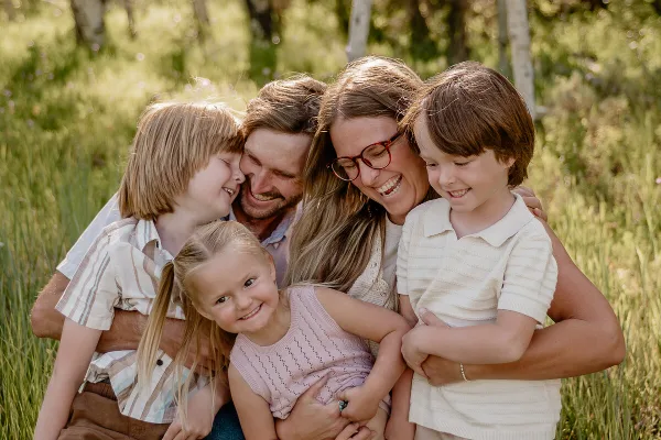 A professional outdoor family portrait featuring a smiling couple and three children huddled together in a grassy field.