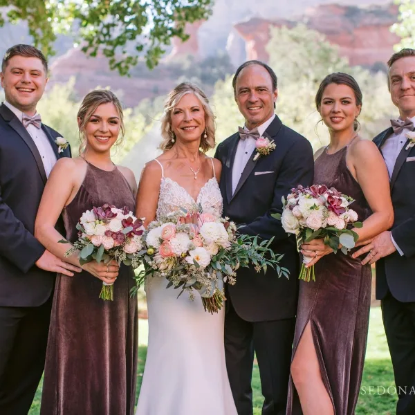 A wedding party posing with floral bouquets and boutonnieres in front of Sedona red rocks.