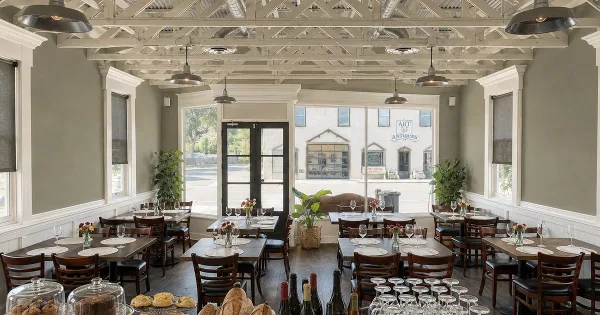 Interior view of a restaurant dining room with wooden tables, chairs, and large windows.