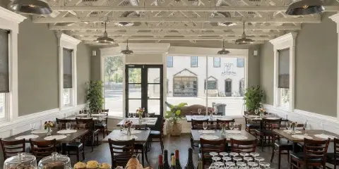 Interior view of a restaurant dining room with wooden tables, chairs, and large windows.