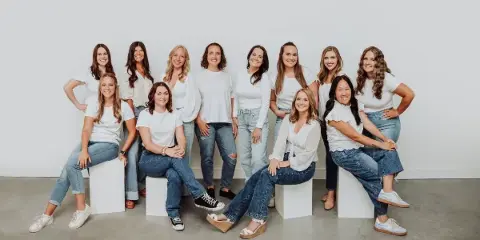 A group of ten women, the wedding coordination team, posing together in a studio setting.
