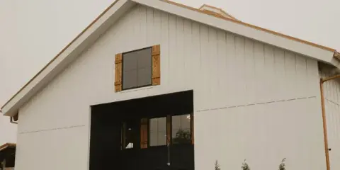 Exterior view of a white barn-style wedding venue with a dark entryway and evergreen trees.