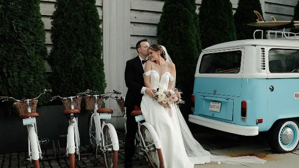 Bride and groom embracing in front of a vintage van and rental bicycles at a wedding venue.