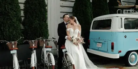 Bride and groom embracing in front of a vintage van and rental bicycles at a wedding venue.