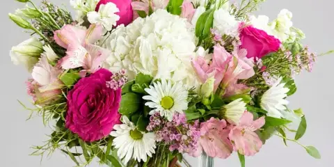 A mixed floral arrangement featuring pink and white roses, alstroemeria, and daisies in a clear square glass vase.