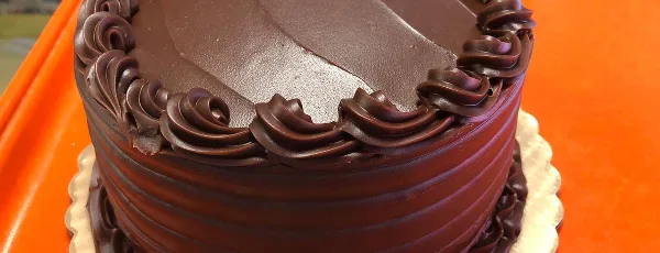 A close-up of a chocolate cake with decorative frosting on an orange table.