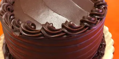 A close-up of a chocolate cake with decorative frosting on an orange table.