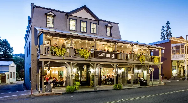 Exterior view of the historic Hotel Sutter building at dusk, showing the two-story structure with a balcony and signage.