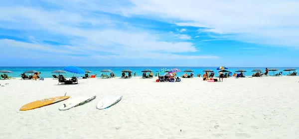 A wide shot of a white sand beach with colorful umbrellas, lounge chairs, and surfboards near the turquoise water.