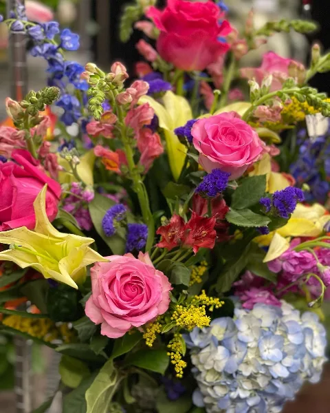 A vibrant floral arrangement featuring pink roses, yellow lilies, blue hydrangeas, and purple filler flowers.