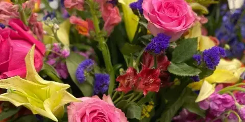 A vibrant floral arrangement featuring pink roses, yellow lilies, blue hydrangeas, and purple filler flowers.