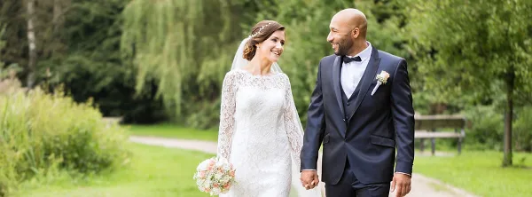 A bride and groom holding hands and smiling at each other in an outdoor park setting.