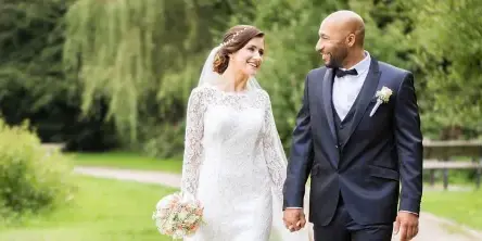 A bride and groom holding hands and smiling at each other in an outdoor park setting.