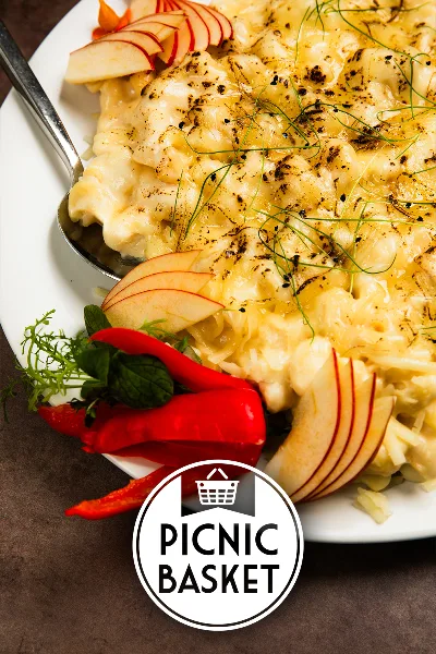 A plated catering dish featuring creamy food, apple slices, red peppers, and herbs with a serving spoon.
