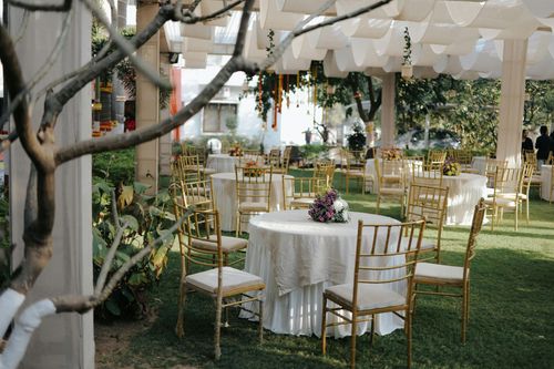 Outdoor event venue with round tables, gold chairs, and floral centerpieces under a white canopy.