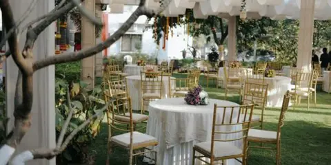 Outdoor event venue with round tables, gold chairs, and floral centerpieces under a white canopy.