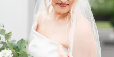 A bride with styled blonde hair and makeup holding a bouquet of white flowers and greenery.