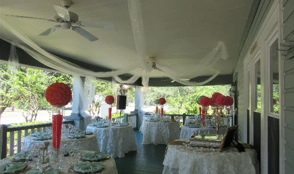 Wedding reception tables set on a covered porch with floral centerpieces and white drapery.