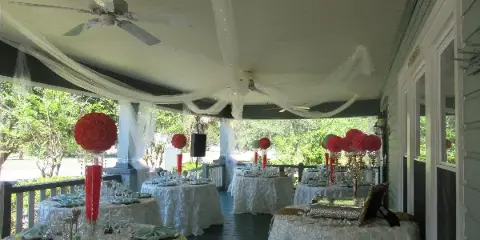 Wedding reception tables set on a covered porch with floral centerpieces and white drapery.