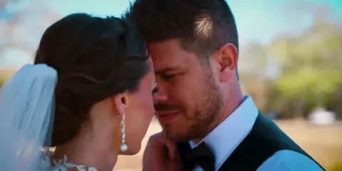 A close-up photograph of a bride and groom sharing an intimate moment, with the bride wearing a veil and the groom in a suit and bow tie.