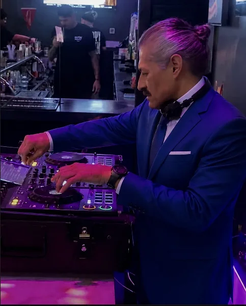 A professional DJ in a blue suit mixing music on a Pioneer controller at a live event.