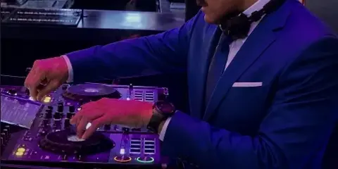 A professional DJ in a blue suit mixing music on a Pioneer controller at a live event.