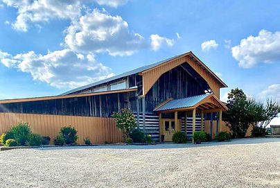 Exterior view of a large rustic barn with a metal roof and wooden siding under a blue sky.