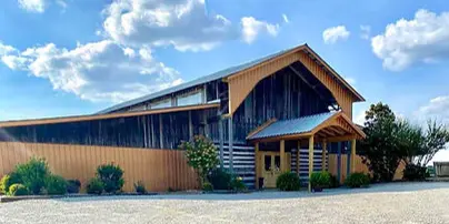 Exterior view of a large rustic barn with a metal roof and wooden siding under a blue sky.